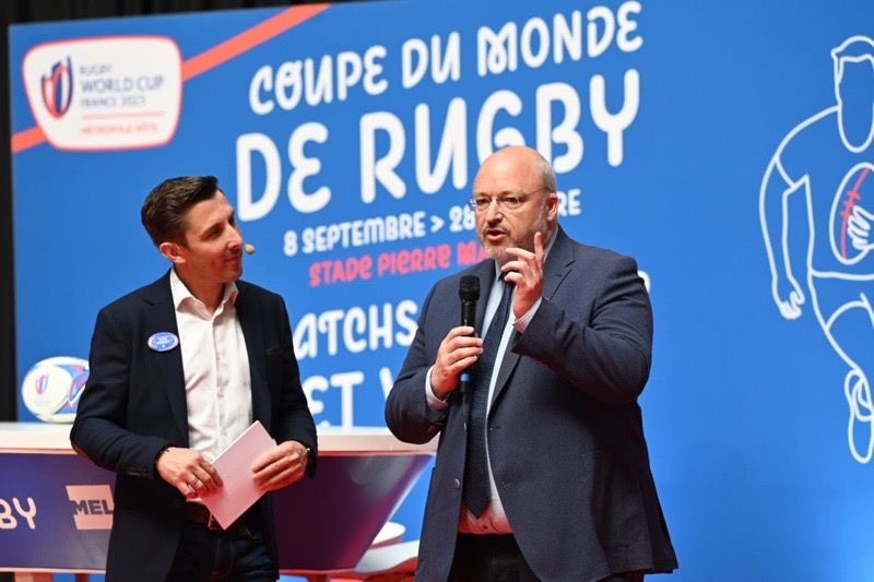 José Freitas sur scène devant l'affiche de la Coupe du monde de rugby, aux côtés d'un intervenant